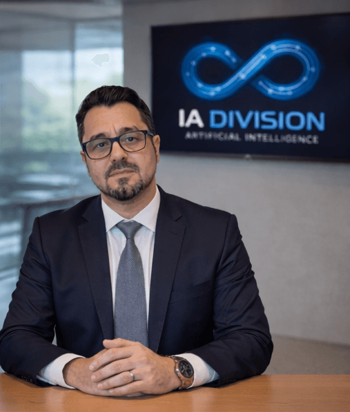 Luis Miguel González, con traje y gafas, en una oficina con el logo de IA Division en la pantalla